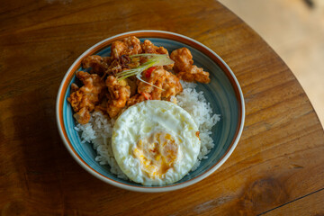 salted egg chicken rice bowl with egg served on blue bowl, over wooden table surface, in cafe environment