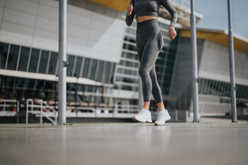 Obraz premium A modern woman in active wear is running outside near a contemporary building, showcasing an urban fitness lifestyle.