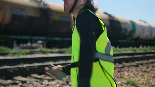 Funny railway engineer dancing and raising his arms while holding a phone in a green uniform. Mid shot.