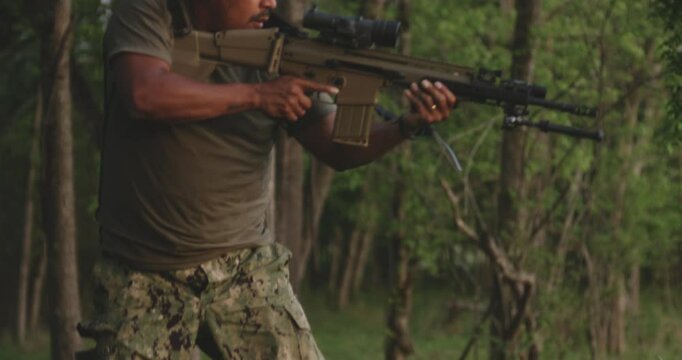 Designated marksman hidden in the forest, aiming a FN Herstal SCAR 17 rifle.