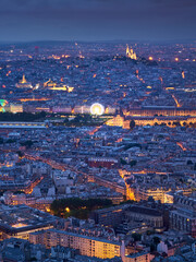 Paris aerial view at twilight toward Monmartre and Sacré-Coeur across Left Bank rooftops and illuminated landmarks. France