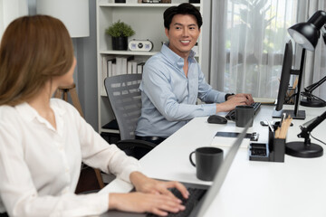 Smiling Asian man talking with woman colleague in planning marketing report project on laptop...