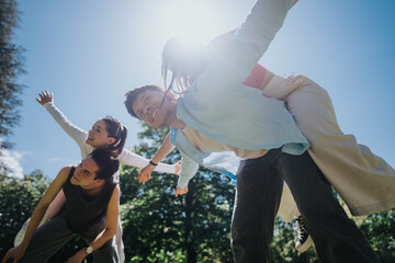 Group of friends having fun in the park, with piggyback rides under the sun, showcasing joy and togetherness. - Powered by Adobe