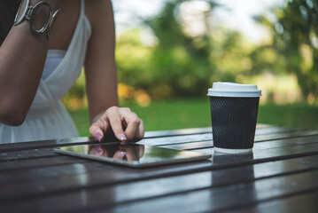 Asian Woman use smartphone drinking coffee hand holding hot disposable cup in green park. Banner Happy Relax asian woman smiling face at outdoors garden. Young women enjoy nature with copy space