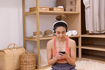 Happy asian woman use headphones listen to music from smartphone outdoor sitting on cozy sofa in living room at home. Music mental therapist for relaxation woman. Leisure cheerful wellness woman