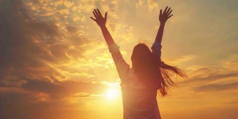 A silhouette of a woman raising her arms in joy as the sun sets behind her, casting a warm glow over the sky