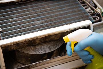 Latex gloved hand applying spray to kill black mold and clean window air conditioning unit.