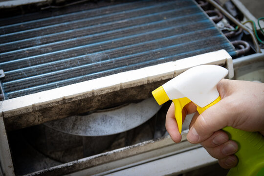 Applying spray to kill black mold and clean window air conditioning unit.