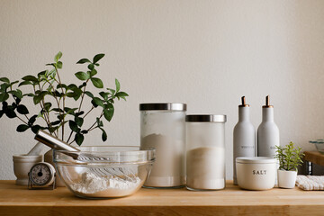 A neatly arranged kitchen countertop with a glass bowl of flour with a whisk, kitchen container on wooden table top for cooking or baking preparation.
