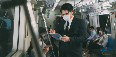 Asian business man wearing protective face mask wathching on digital tablet, Hand holding on a handrail in public subway travel to work