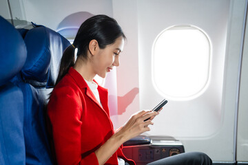 A woman in a formal suit sits in a window seat of an economy class section, looking out the airplane window, ready for her business journey.