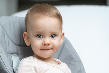 Close-up of a toddler baby gazing at the camera with calm face sitting in high chair