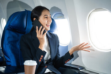 Fototapeta premium A woman in a formal suit sits in a window seat of an economy class section, looking out the airplane window, ready for her business journey.