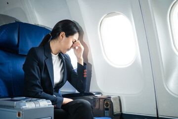 A woman in a formal suit sits in a window seat of an economy class section, looking out the airplane window, ready for her business journey.