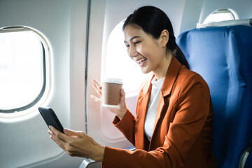 Fototapeta premium A woman in a formal suit sits in a window seat of an economy class section, looking out the airplane window, ready for her business journey.