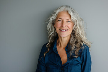 Fototapeta premium A woman with long, gray, wavy hair smiles at the camera while wearing a blue shirt