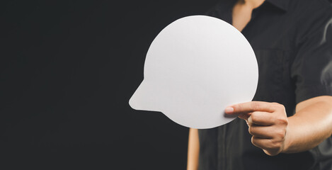 Businessman holding a blank white speech bubble while standing on a black background.