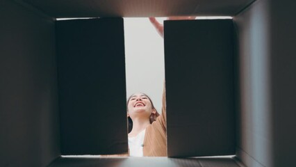 Low angle view of surprised young asian woman unpacking. Opening carton box and looking inside. Packaging box, delivery service. Human emotions and facial expression