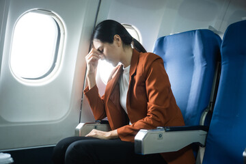 A young Asian woman, an airplane passenger, sits by the window seat, experiencing nausea and...