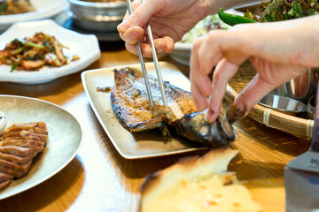 식탁 위에서 반찬과 고등어 구이를 밥과 함께 맛있게 먹고 있는 모습