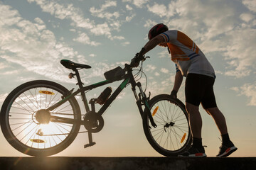 Man cyclist repairing a bike against the background of sky