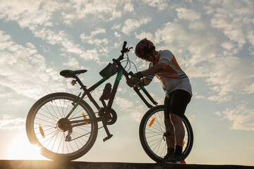 Naklejka premium Man cyclist repairing a bike against the background of sky
