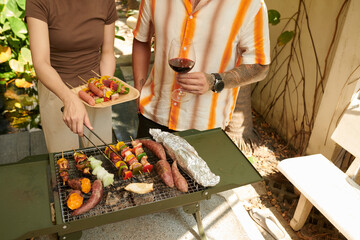 Cropped image of couple drinking wine and grilling kebabs outdoors