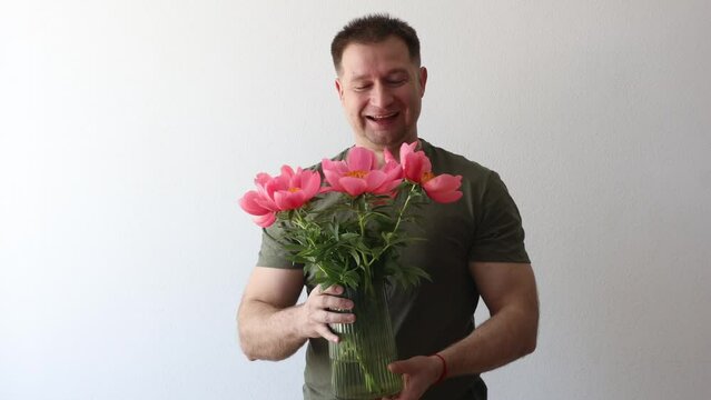 A man in a hacky t-shirt holds a vase of peonies and points to the camera