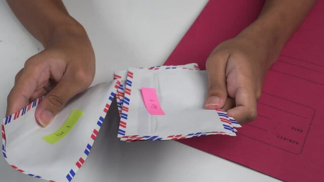 hands sorting envelopes on table with red document folder