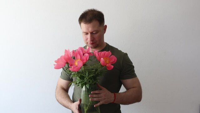 A man in a hacky t-shirt holds a vase of peonies and points to the camera
