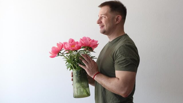 A man in a hacky t-shirt holds a vase of peonies and points to the camera