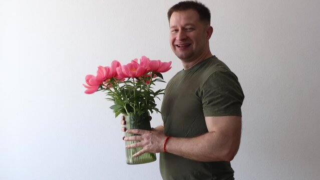 A man in a hacky t-shirt holds a vase of peonies and points to the camera