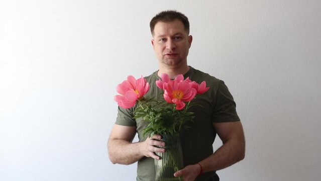 A man in a hacky t-shirt holds a vase of peonies and points to the camera