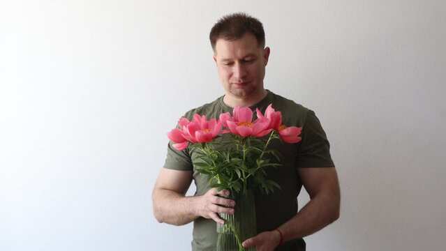 A man in a hacky t-shirt holds a vase of peonies and points to the camera