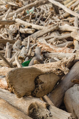 A pile of weathered pieces of driftwood, varying in size and shape, scattered and intertwined with each other. The wood looks aged and sun-bleached. Debris washed ashore by the sea.