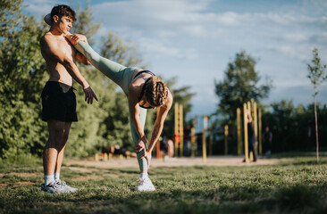 A young man helps a woman with a stretching exercise in an outdoor fitness park. Emphasis on...