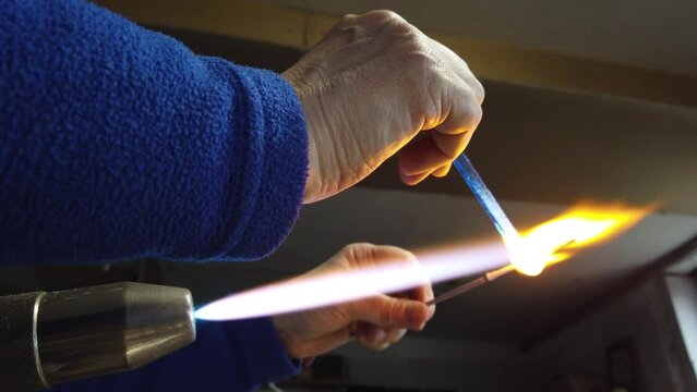   Close up of artist hands creating glass pendant with lampworking technique. Shaping glass with flame making jewelry using gas burner