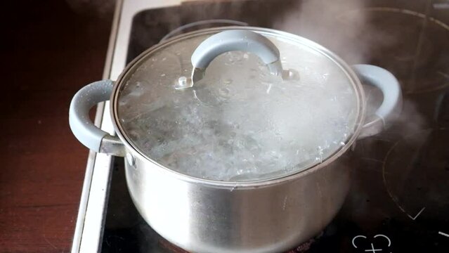 There is water boiling in a saucepan on the stove. Steam is coming out, the lid is bouncing