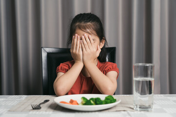 Little cute kid girl refusing to eat healthy vegetables. Children do not like to eat vegetables.