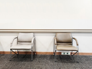 Two sleek, modern chairs with metal legs and cushioned seats sit side by side in a minimalist waiting room with a plain and simplistic light grey wall, exuding a calm, chic and stylish vibe.