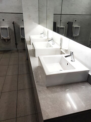 A row of white marble sinks in a public toilet gleams under bright lights. Each sink has a modern faucet and a large mirror above. The clean, elegant design emphasizes a polished, hygienic environment