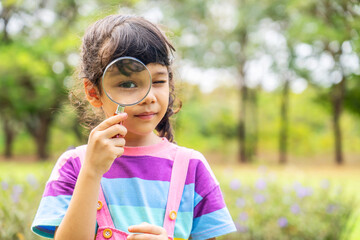 Image of little girl exploring the nature with magnifying glass outdoors, Child playing in the park with magnifying glass. Curious kid exploring nature by magnifier