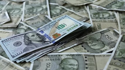 One hundred american dollars banknotes falling on five hundred indian rupees background.