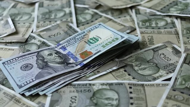 One hundred american dollars banknotes falling on five hundred indian rupees background.