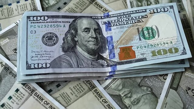 One hundred american dollars banknotes falling on five hundred indian rupees background.