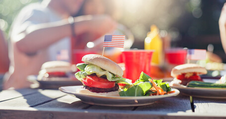 Hamburger, food and salad on plate outdoor at reunion lunch for national independence day. American flag, vegetables and patty on bun by wooden table for United states holiday event in backyard.
