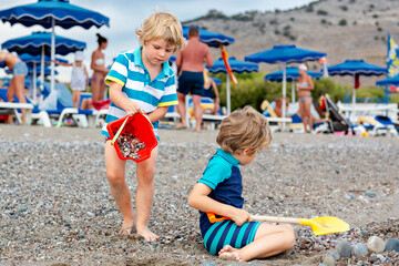 Two little blond kids boys building pebble stone castle on beach. Funny siblings, children playing...