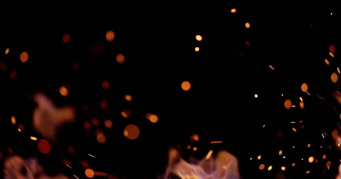 Close-up. Wind blows yellow flames and small glowing sparks from hot coals. Sparks fill all dark space around them and make it light up dark starry sky with millions of bright stars. AD. Copy space.