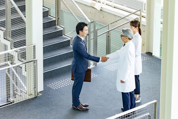 白衣の技術者と握手するビジネスマン