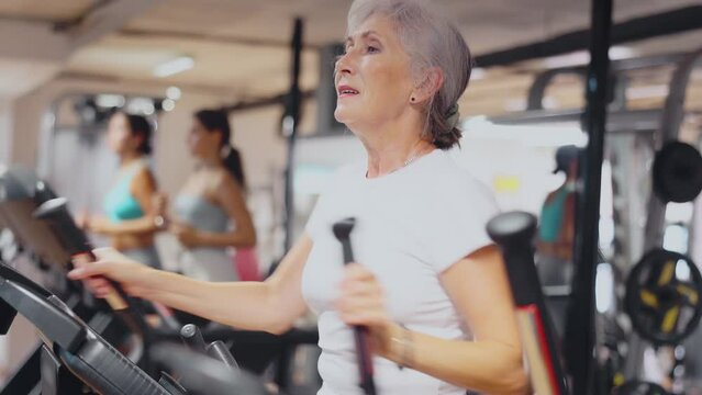 Elderly athletic woman in sportswear training on elliptical machine in gym